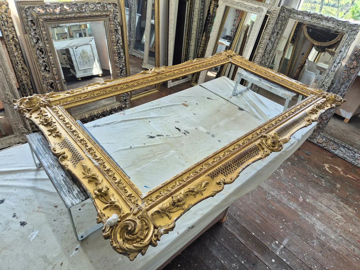 Ein goldener, kunstvoll geschwungener Rahmen liegt auf einer Arbeitsplatte.